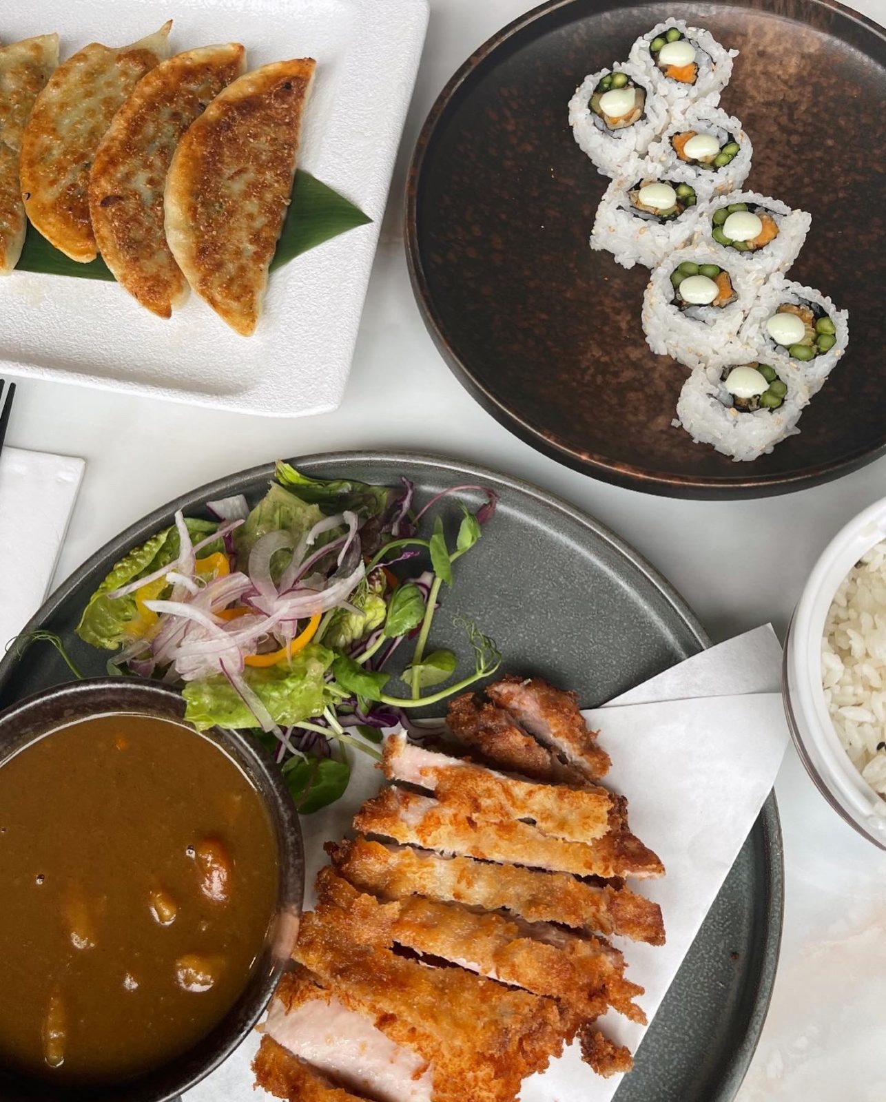 Several dishes from Oba on a table: they include vegetarian sushi, chicken katsu curry and rice, amongst other small dishes