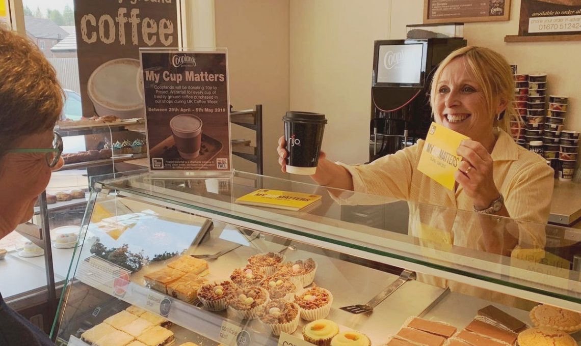 Bakery store assistant is giving a coffee and a leaflet to a customer in a Cooplands store