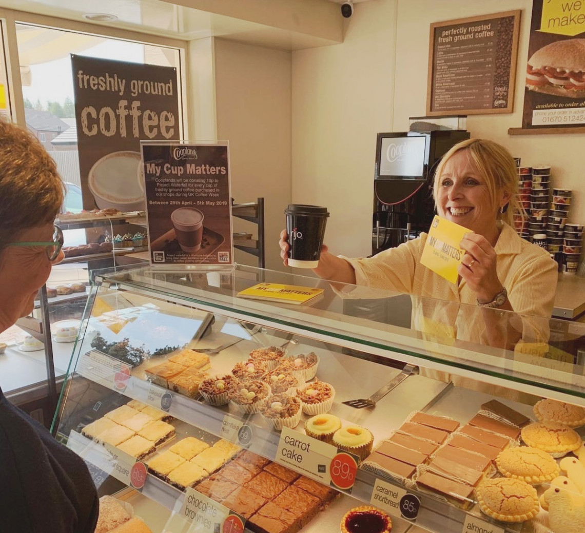 Bakery store assistant is giving a coffee and a leaflet to a customer in a Cooplands store
