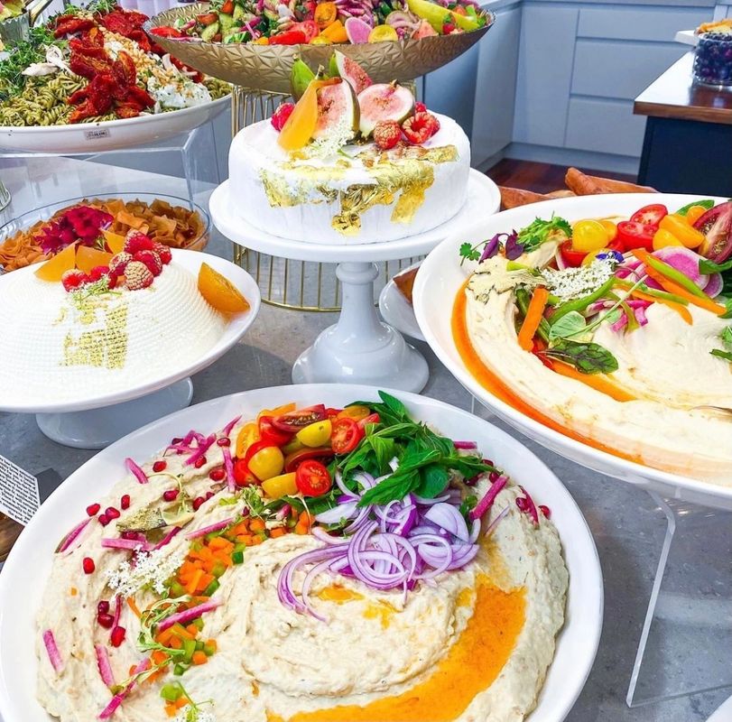 selection of dishes including cakes and hummus with fruit and berries as decoration.