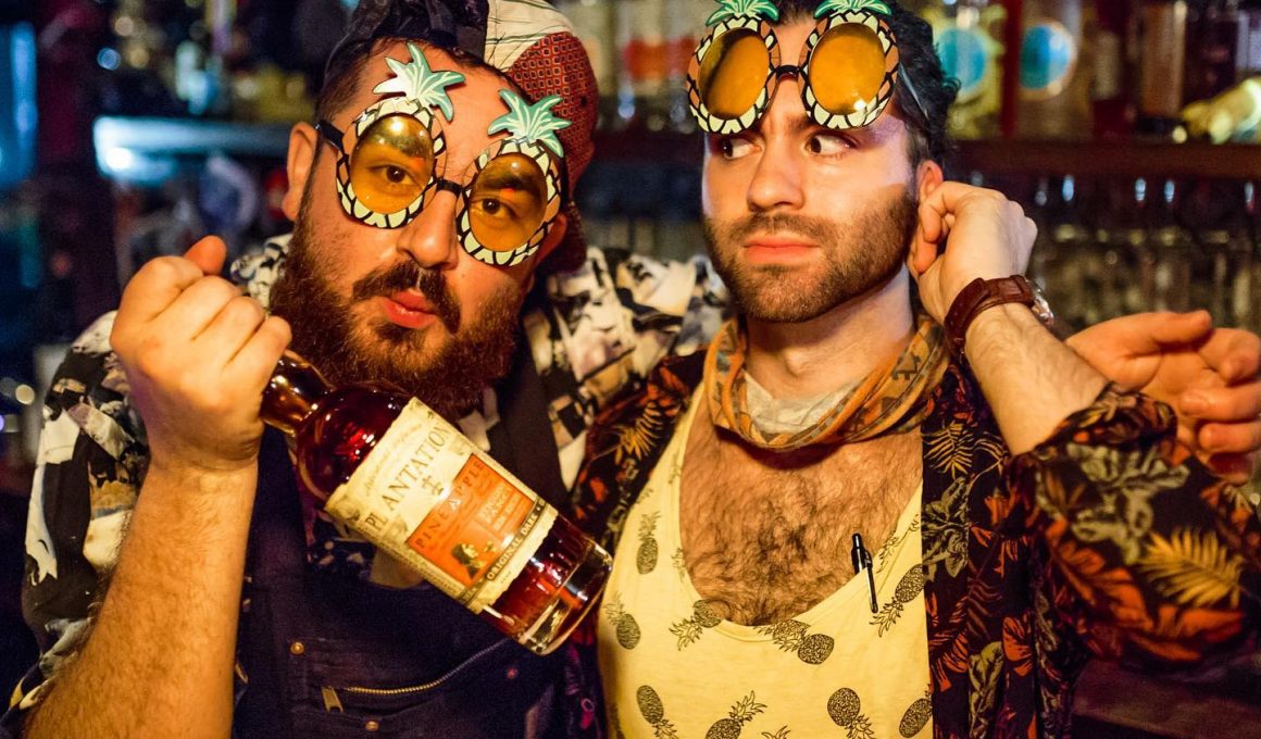 two men with party glasses on and with a bottle of win in their hands