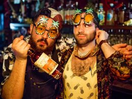 two men with party glasses on and with a bottle of win in their hands