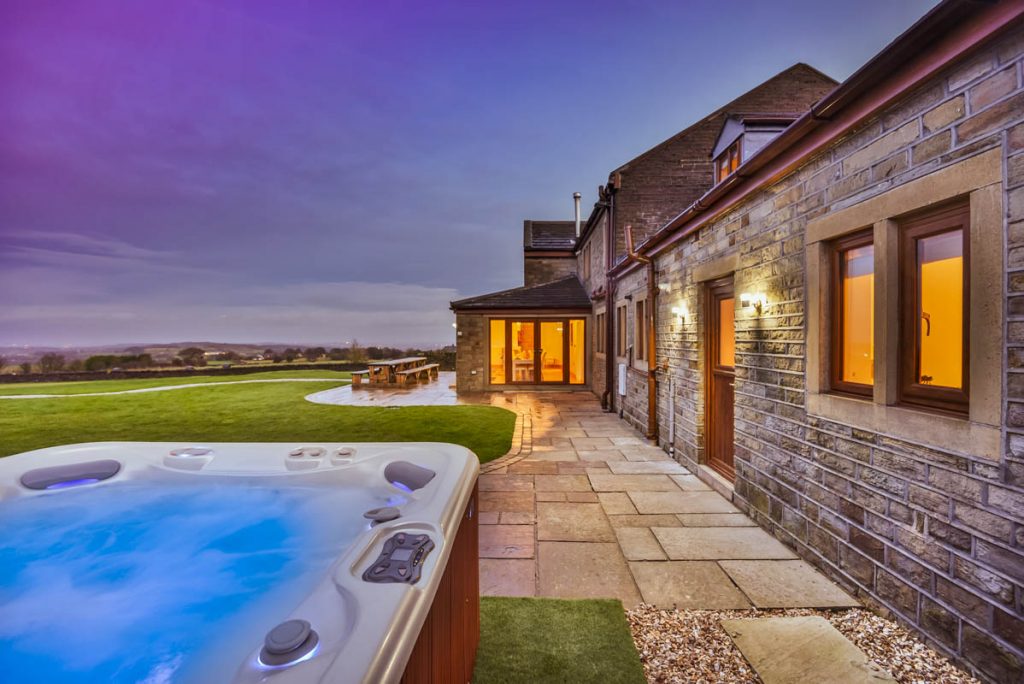 hot tub on a patio with a big barn house to the right.