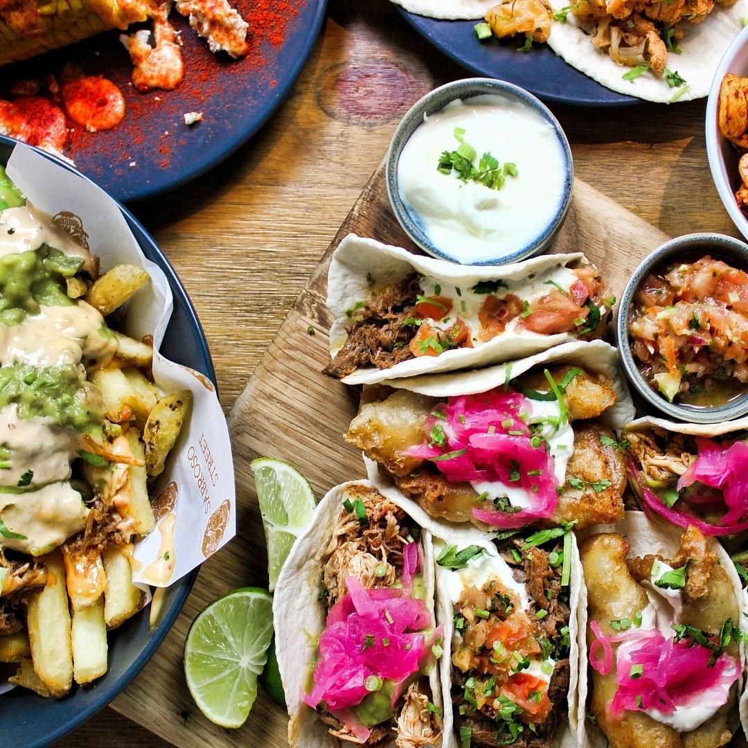 An overhead shot of tacos and other Mexican food on a wooden table.