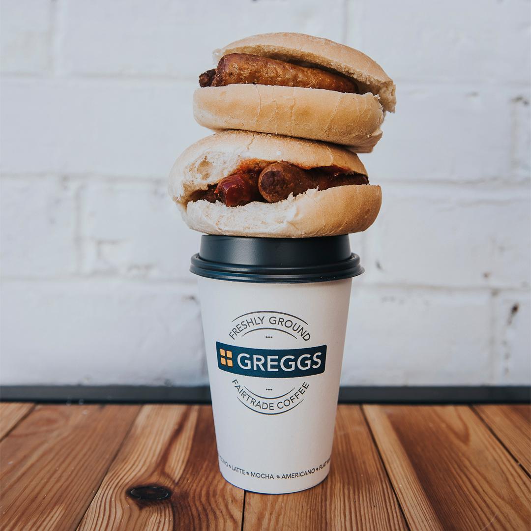 Greggs coffee with sausage sandwich on top.