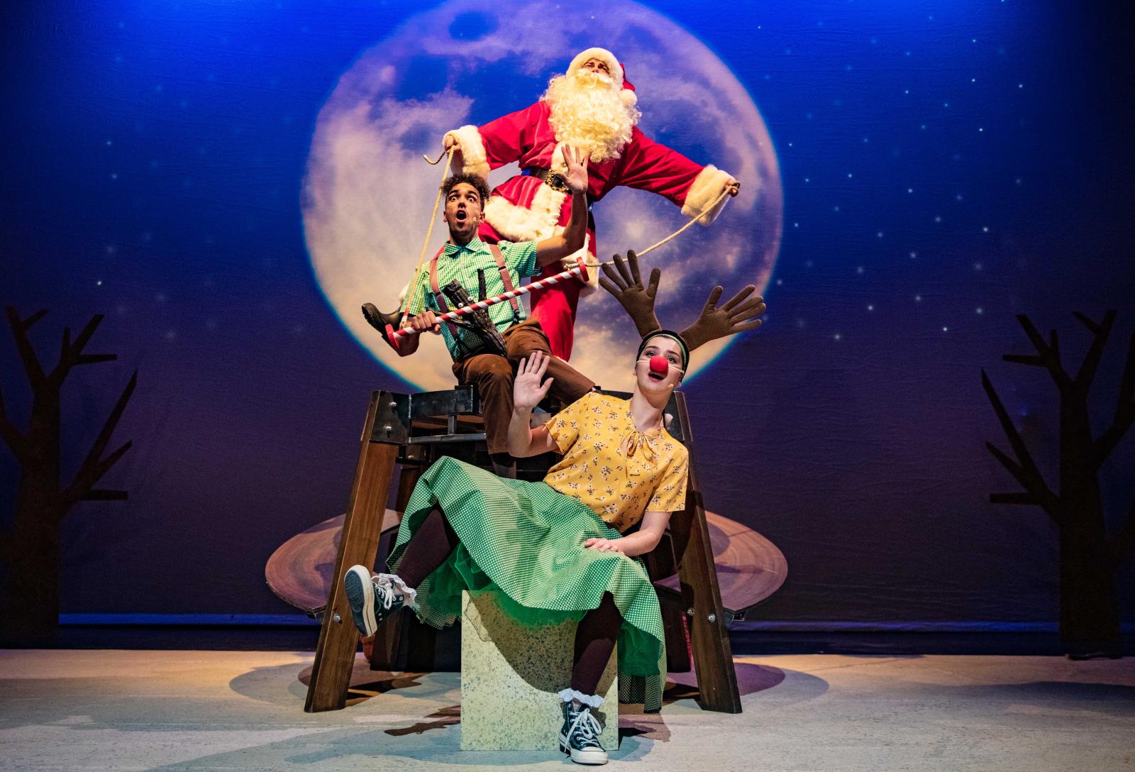 Three actors dancing on stage, including one dressed as Santa Claus.