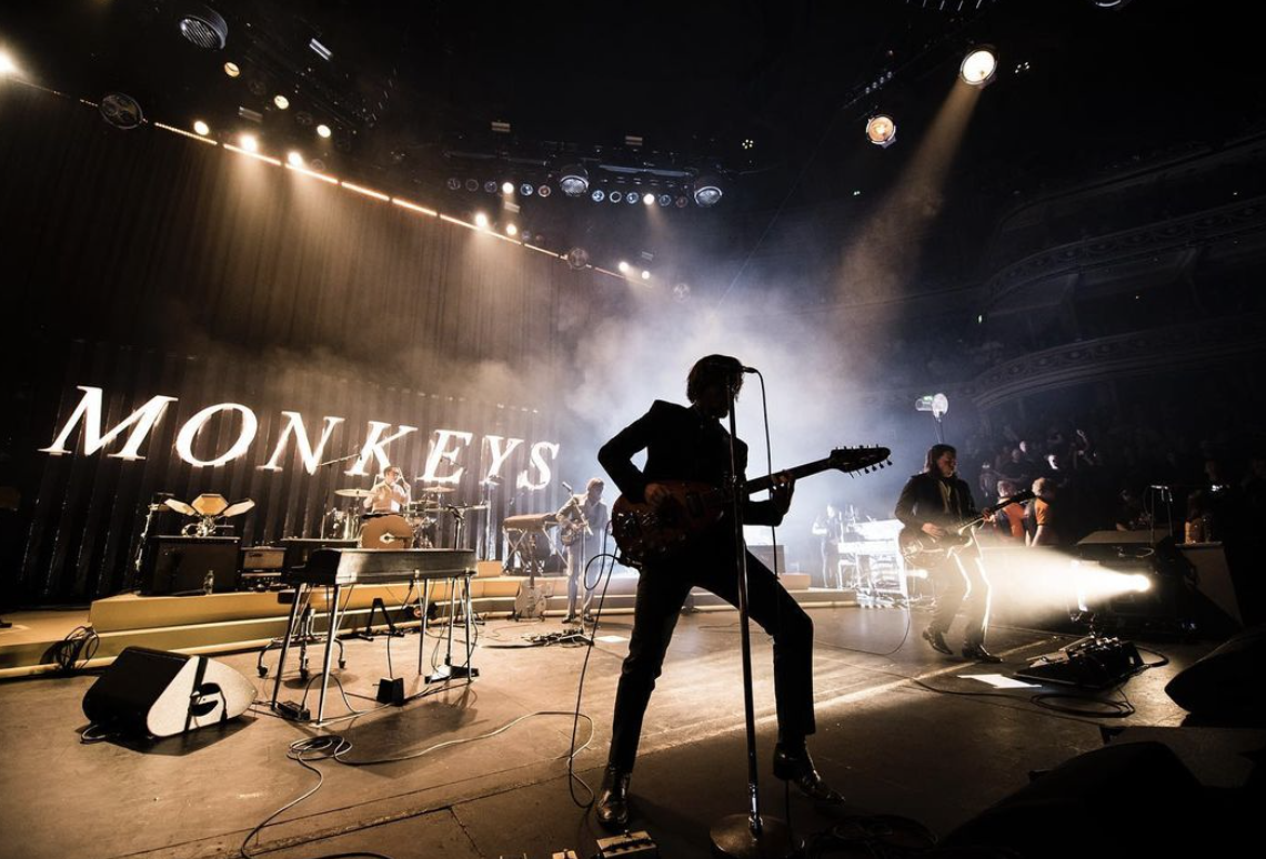 The Arctic Monkeys performing on stage at a music festival. 