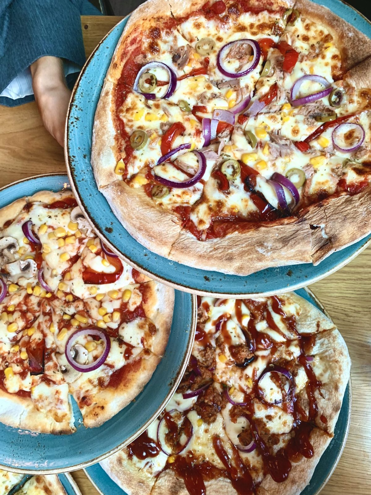 three pizzas held to camera.
