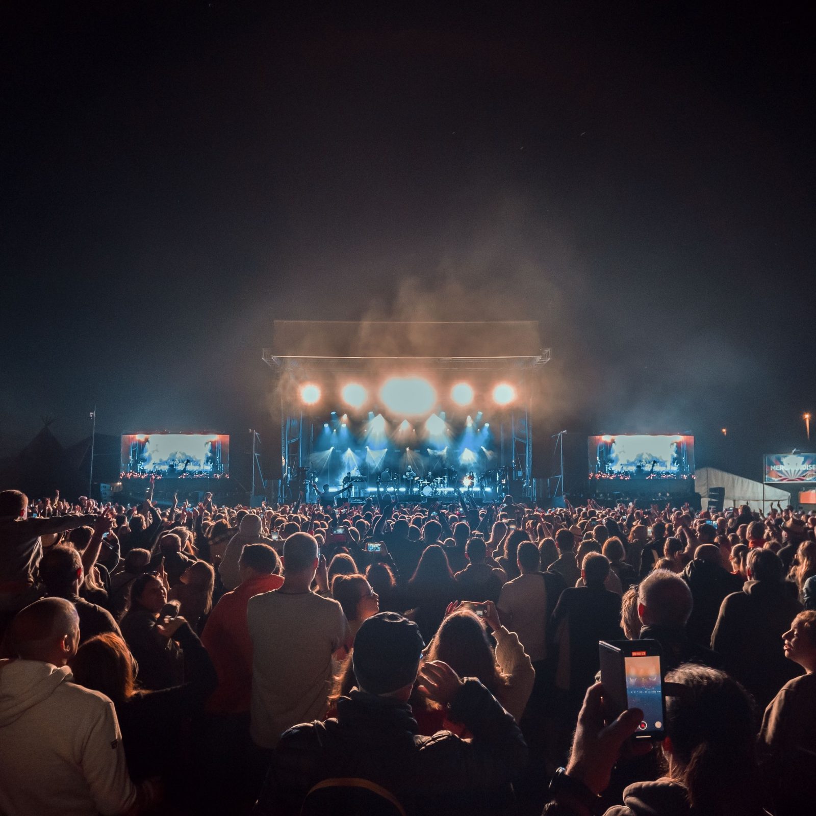 A huge crowd of people watching live music on an outdoor stage. 