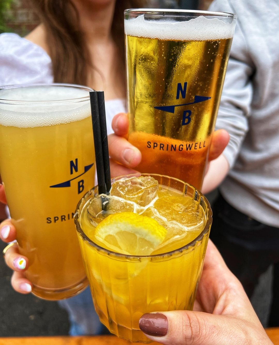 three glasses cheersing with IPA, lager and cocktail.