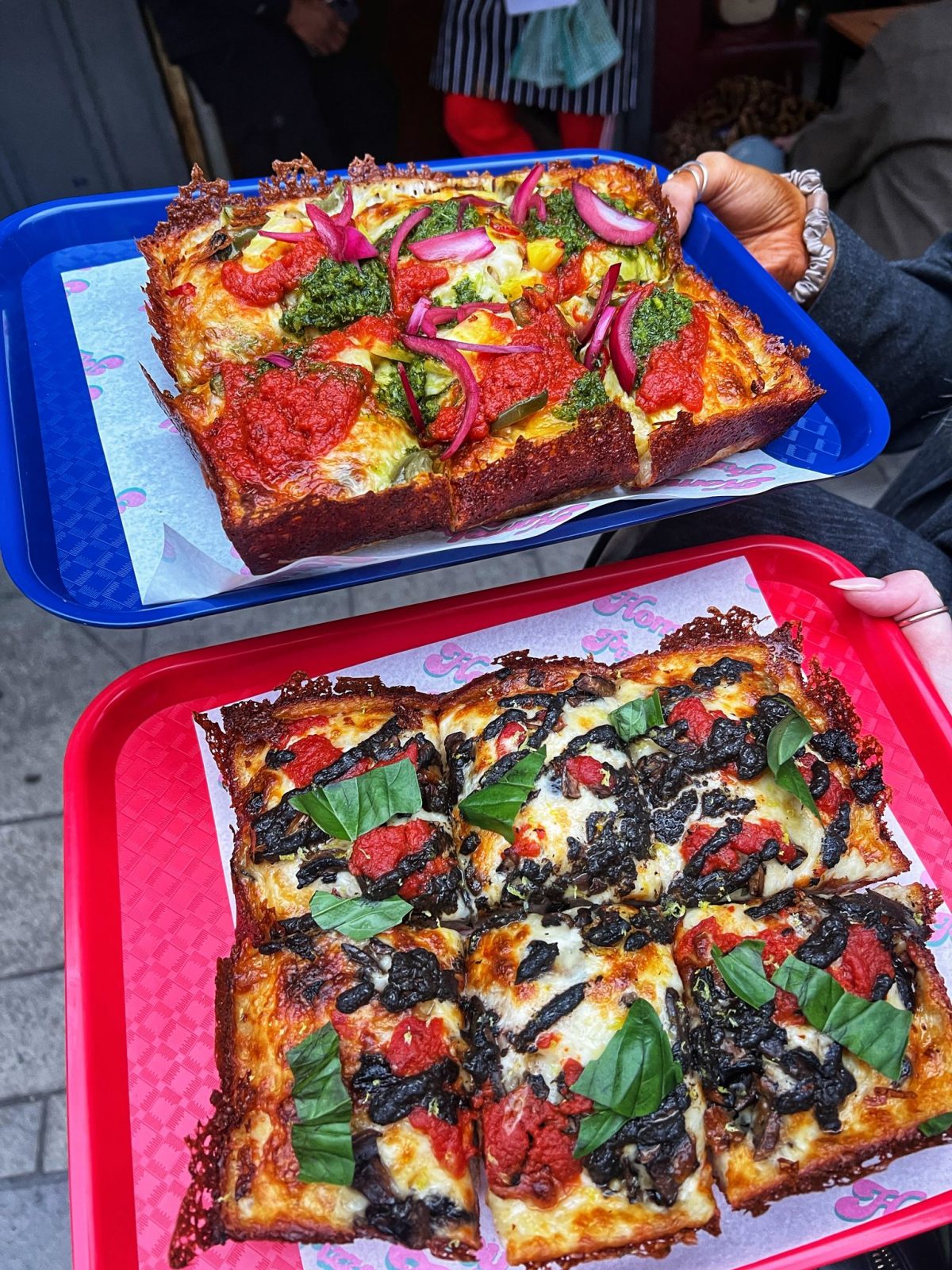 two pizzas being held out on trays.