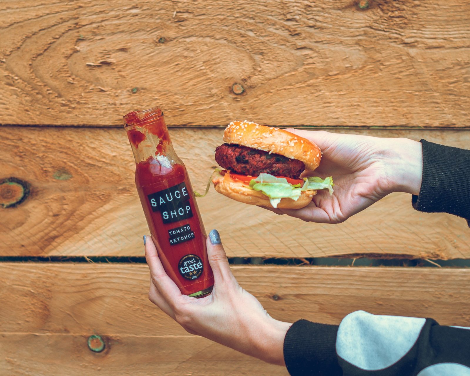 Someone holding up a burger and a bottle of ketchup.