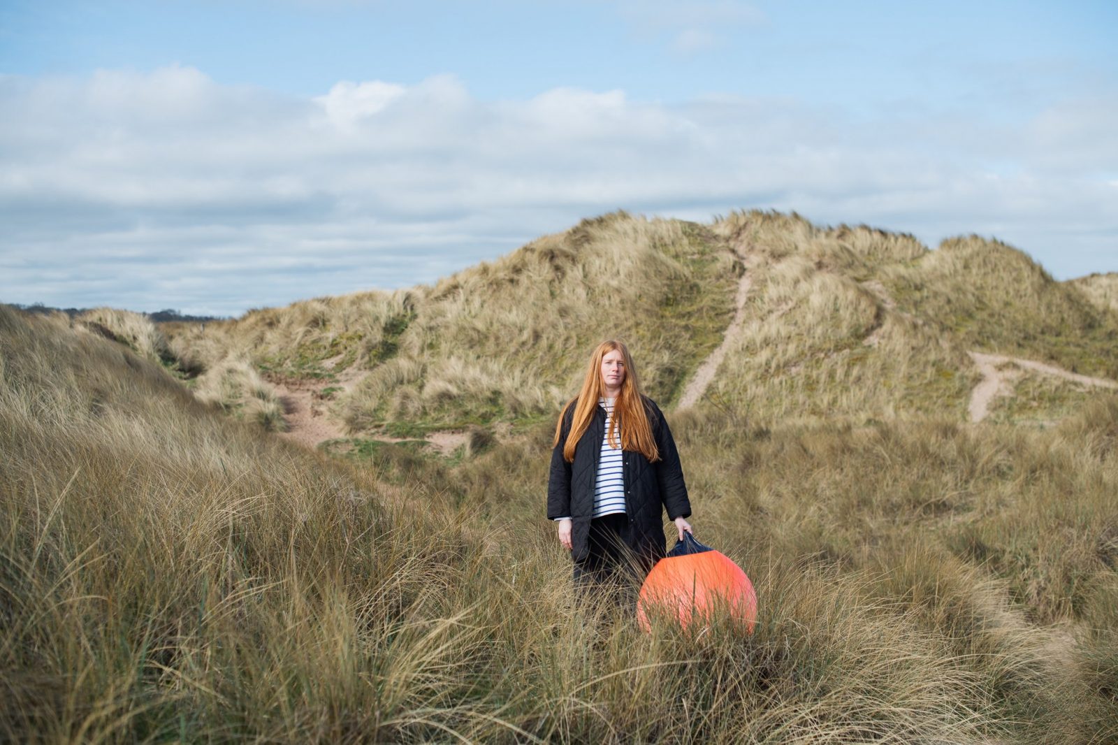 A woman on a hill holding an orange balloon. 