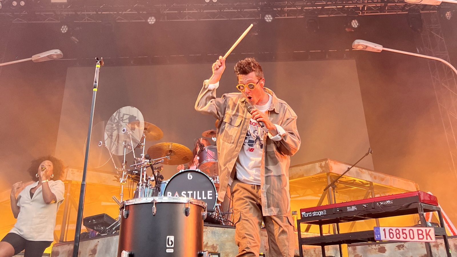 A man singing into a microphone as well as banging a drum.