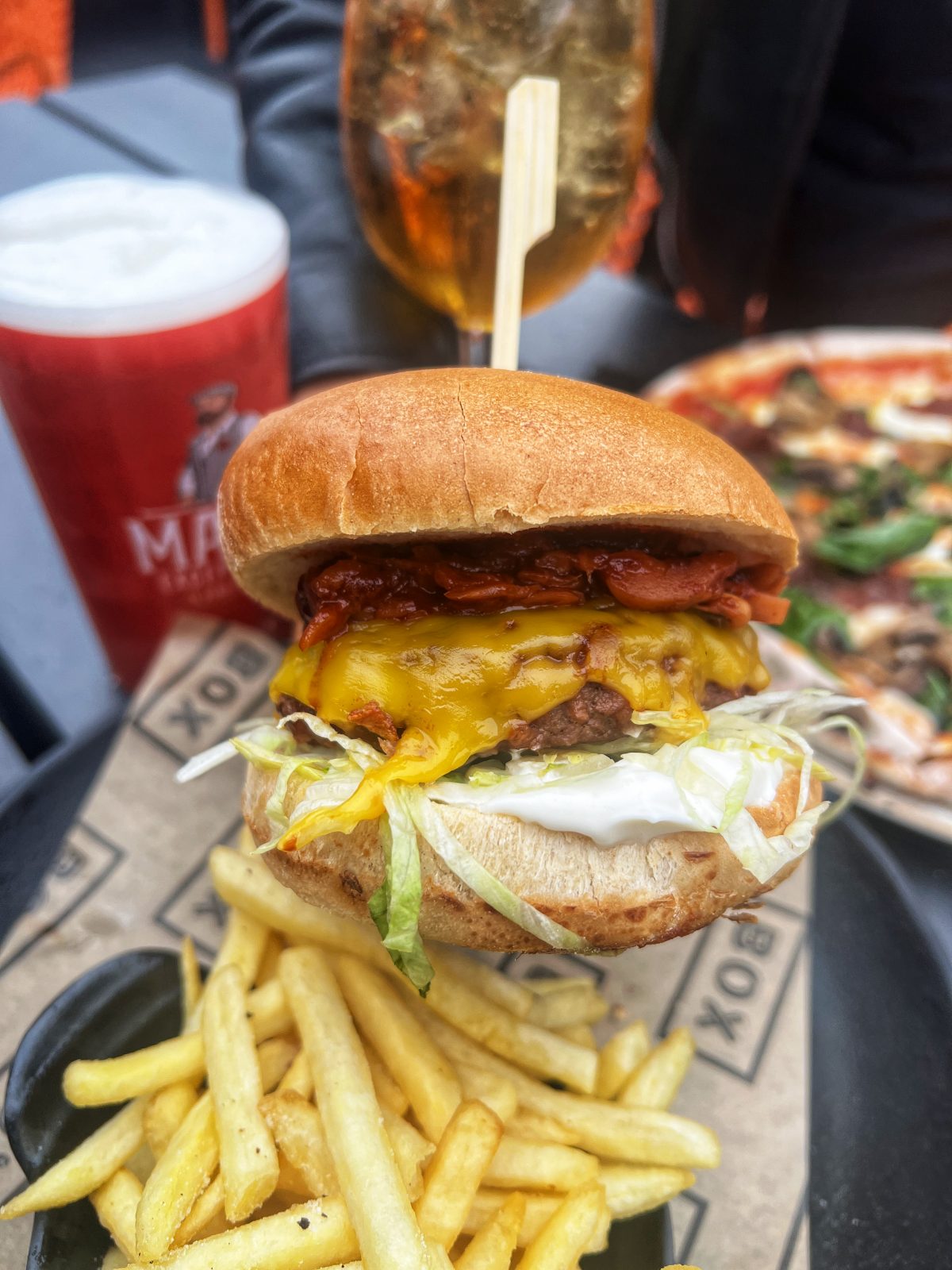 a burger with fries, a pizza and drink in the background.