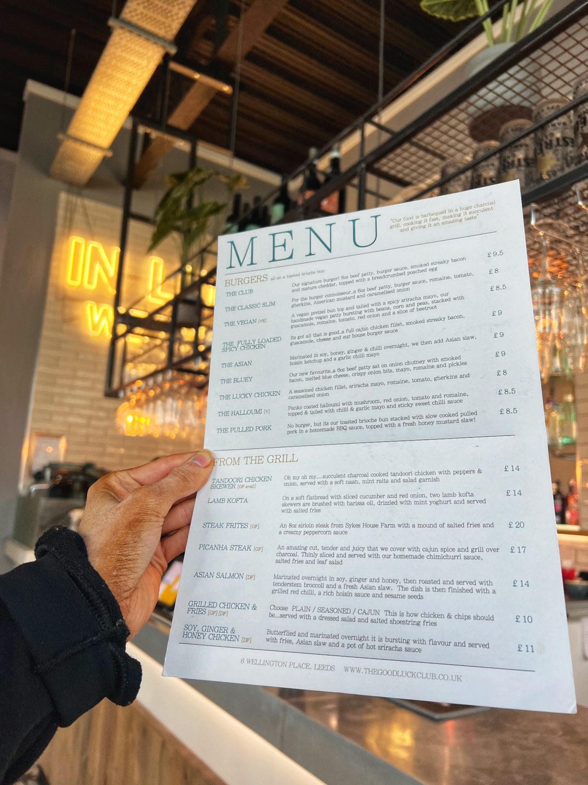 Menu held to camera with yellow neon sign in background.