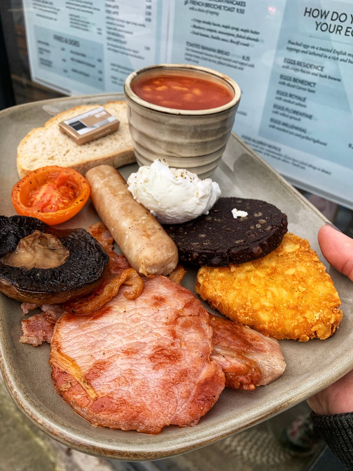 A full English breakfast with bacon, egg, black pudding, hash brown, tomato, mushroom, sausage, beans and bread.