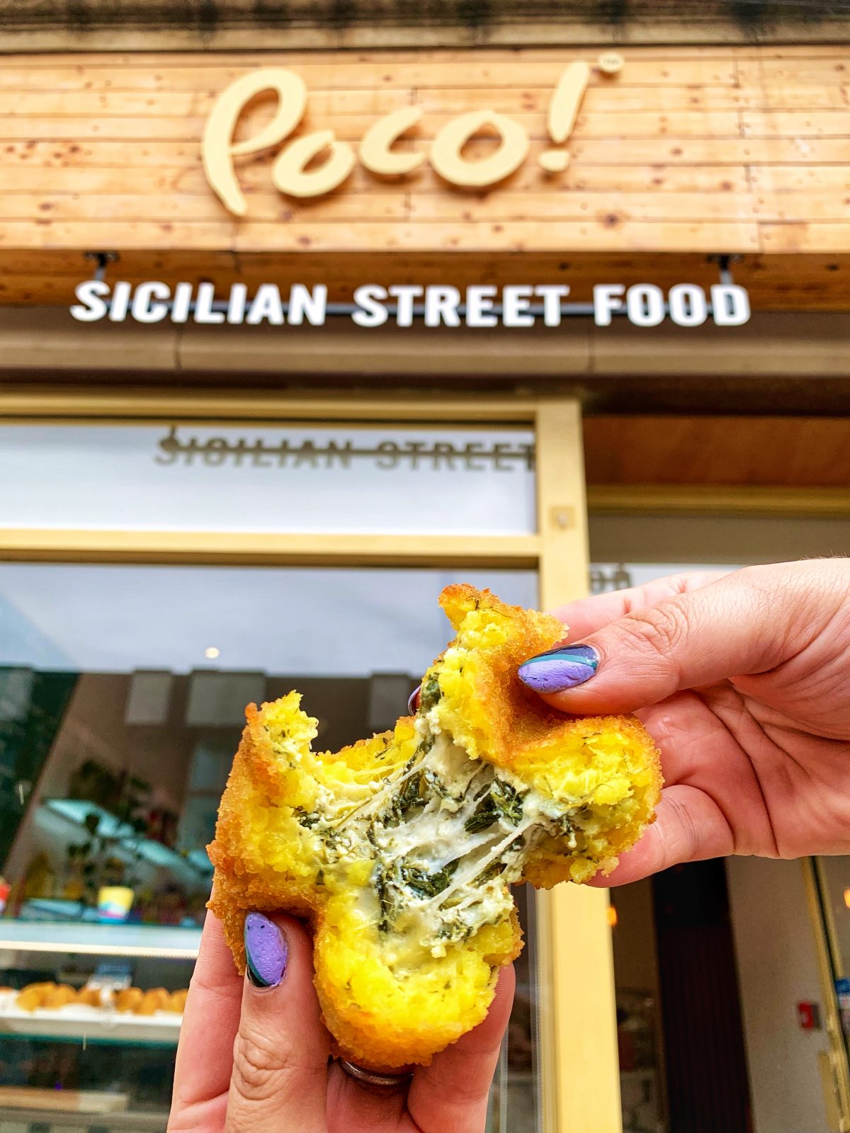 A ball of arancini being pulled apart under a POCO sign.