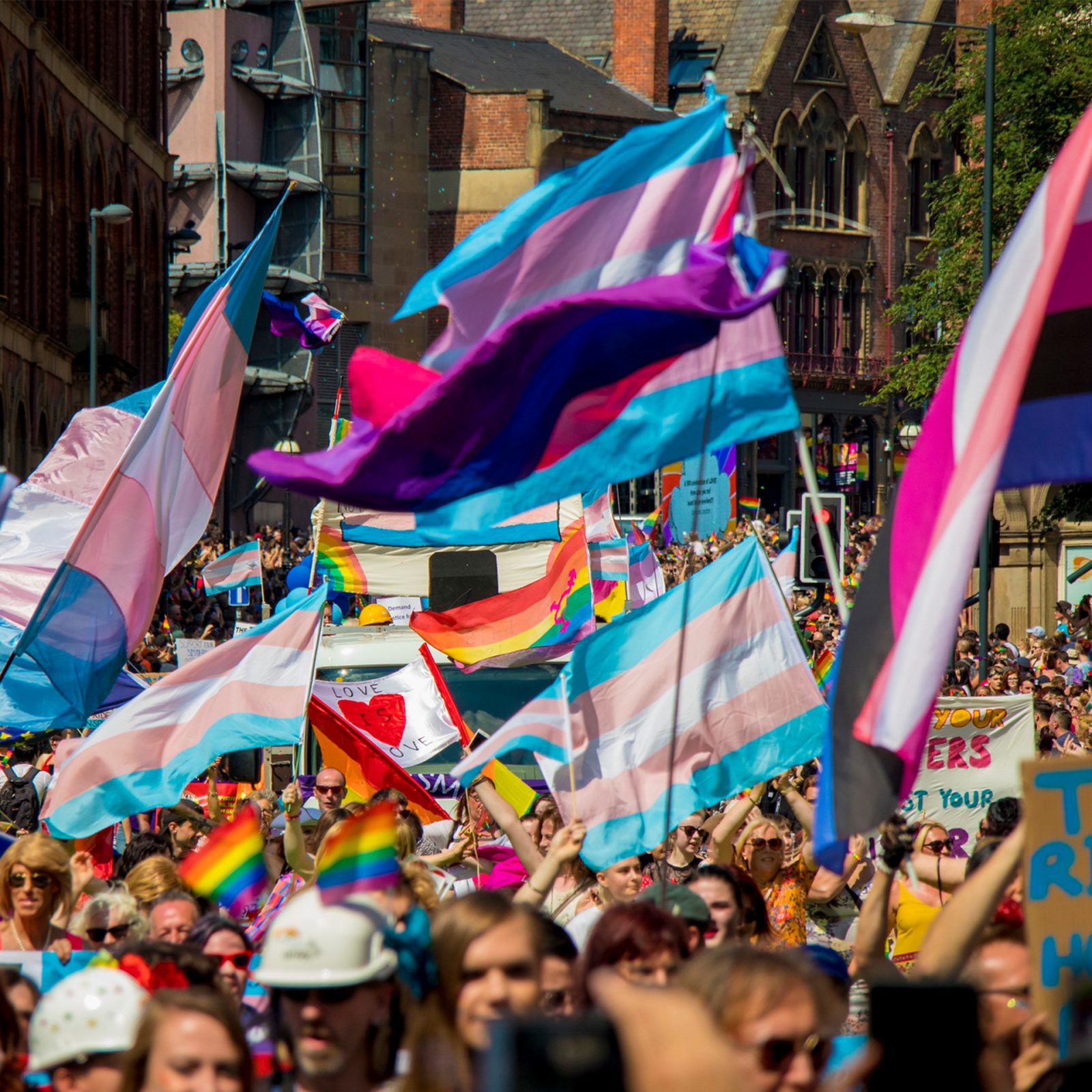 A range of rainbow flags being waved in the air to celebrate Pride. 