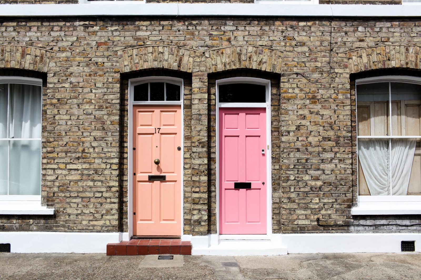 Two pink doors next to one another on a street.