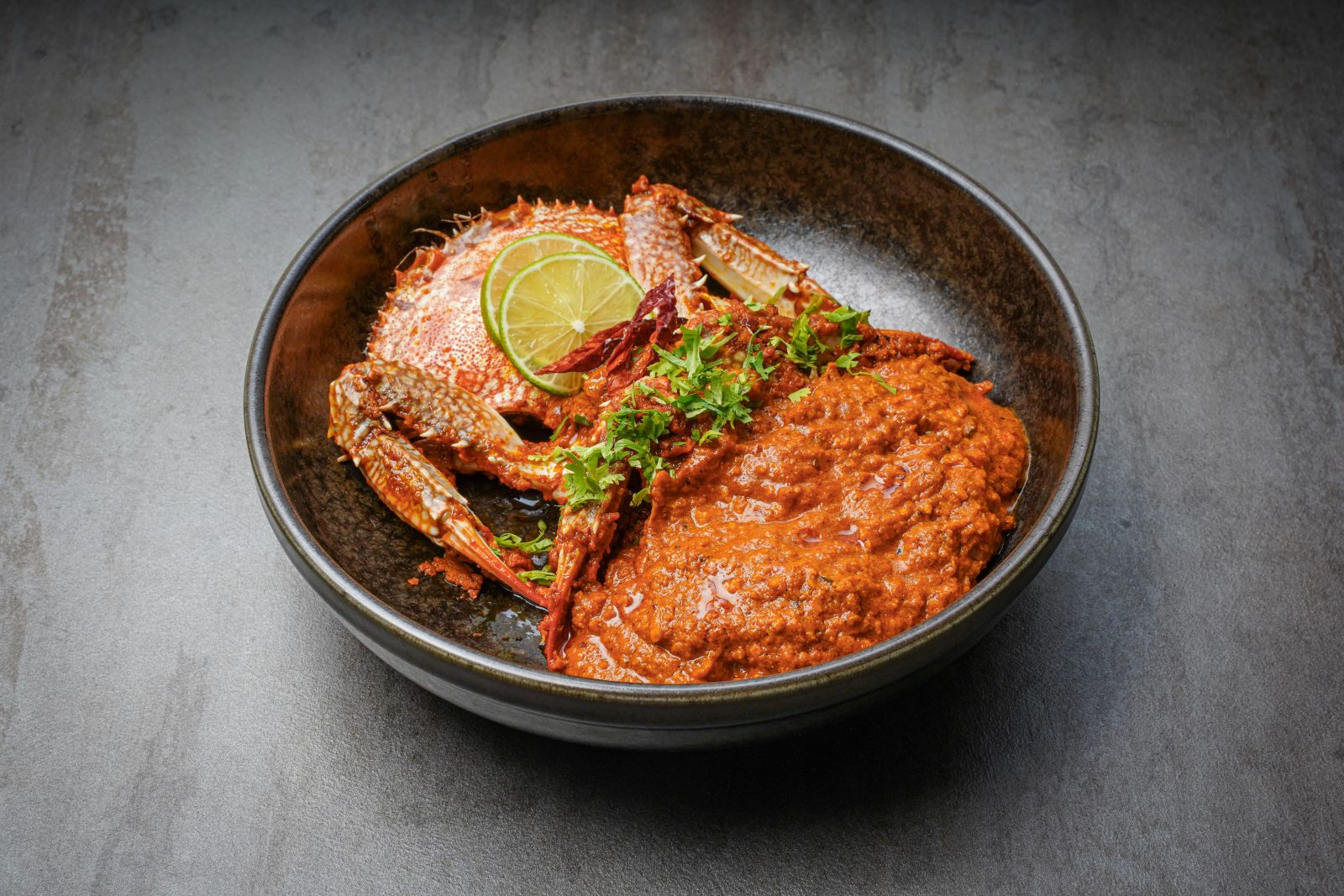 A crab curry in a black bowl.