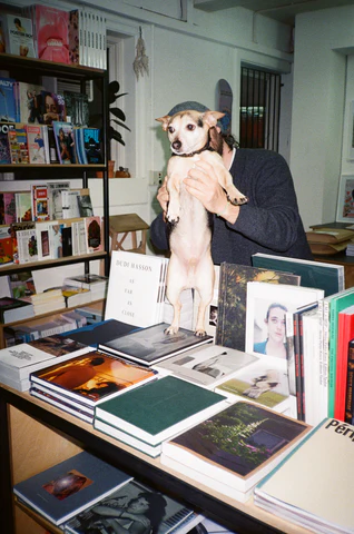 A dog stood on a tabletop covered in books.