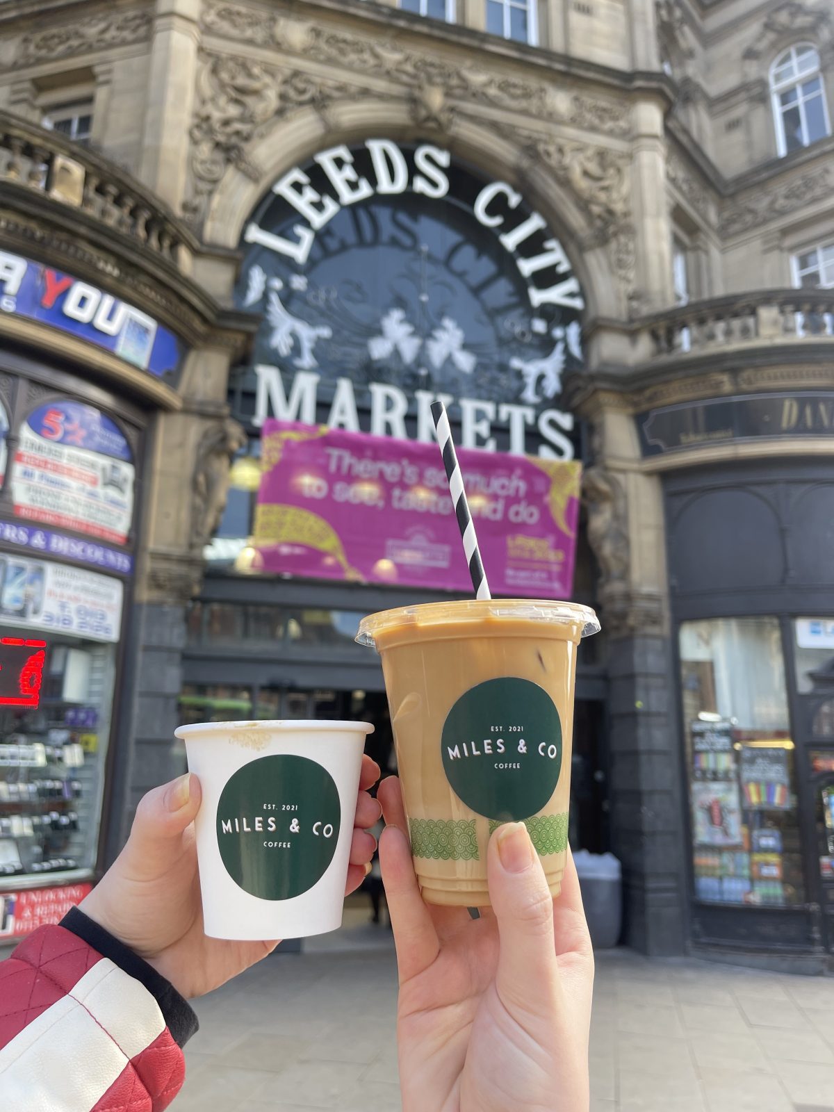 Two coffees being held up outside Leeds Kirkgate Market. 