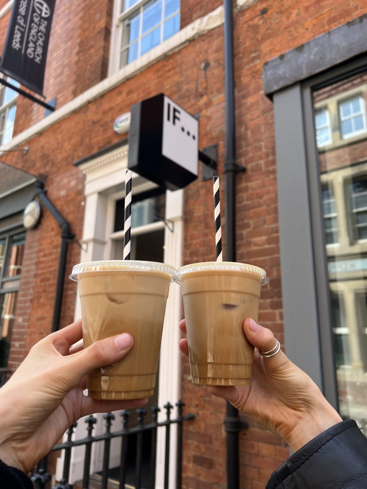 Two coffee cups held in the air outside a sign that reads 'IF...'.