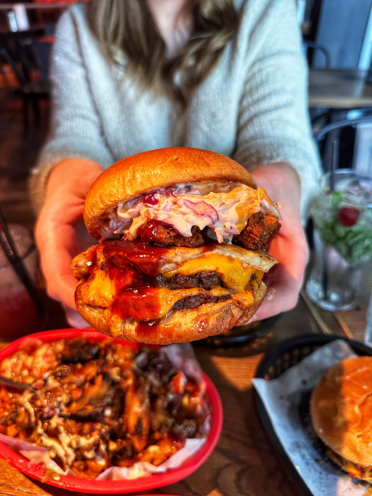 burger held to camera with coleslaw, burger patty and cheese inside.