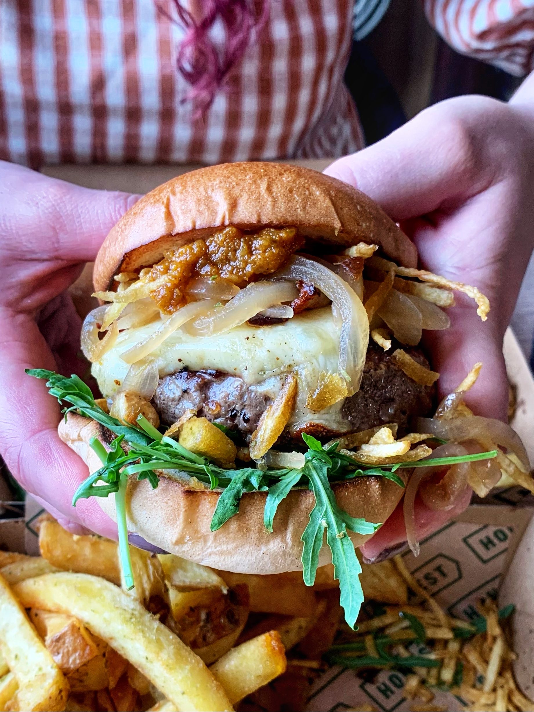 burger held up to camera with cheese, shoestring fries and rocket inside.
