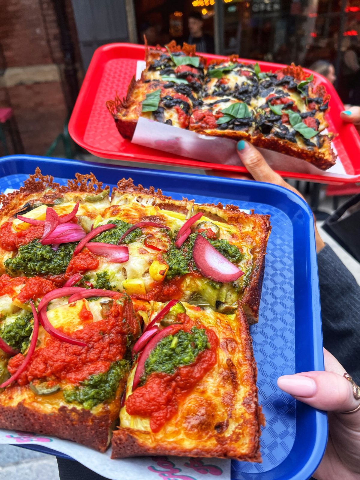 Two Detroit style pizzas on colourful trays. 