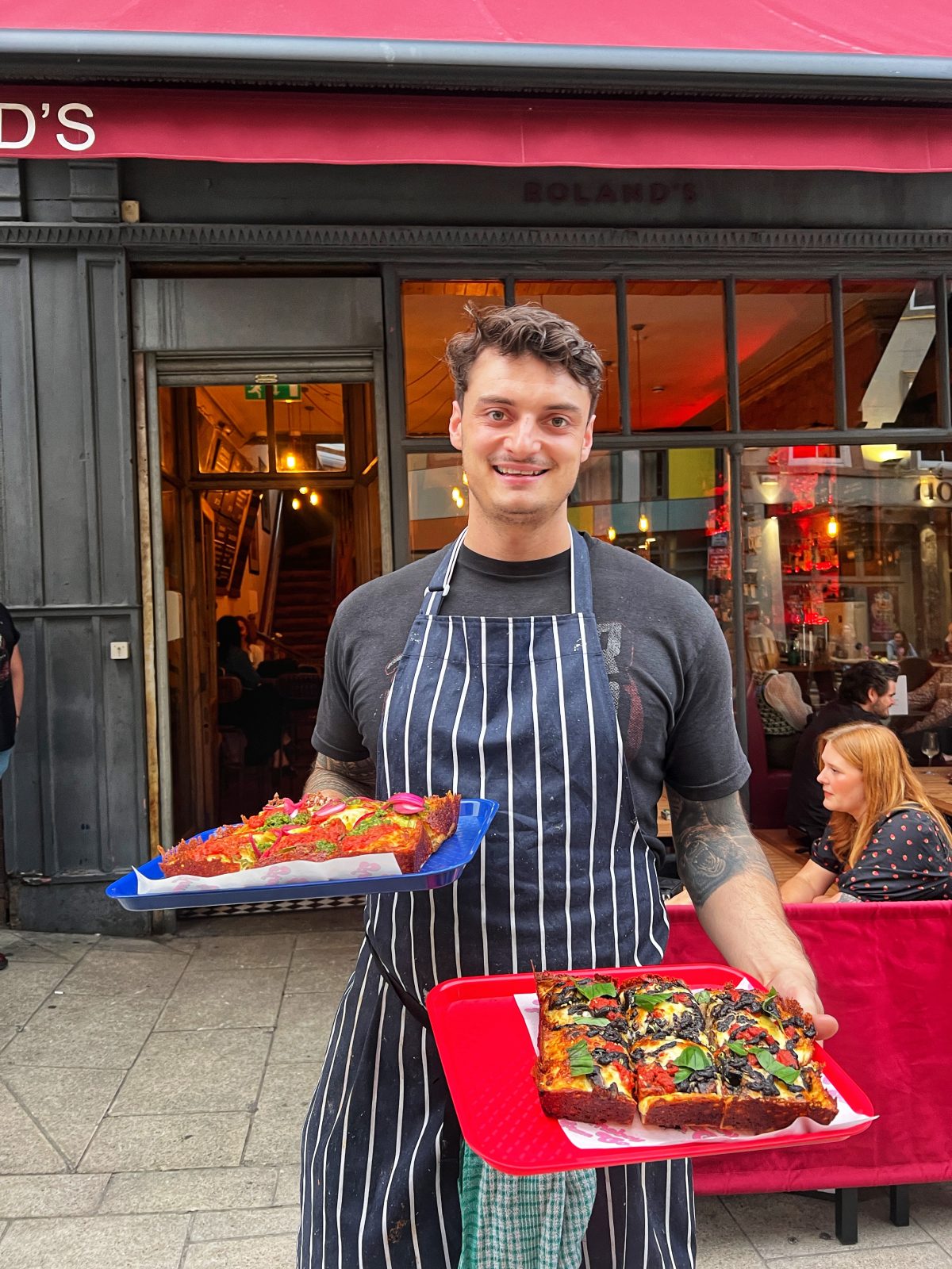 A man with a chef's apron on holding two pizzas. 