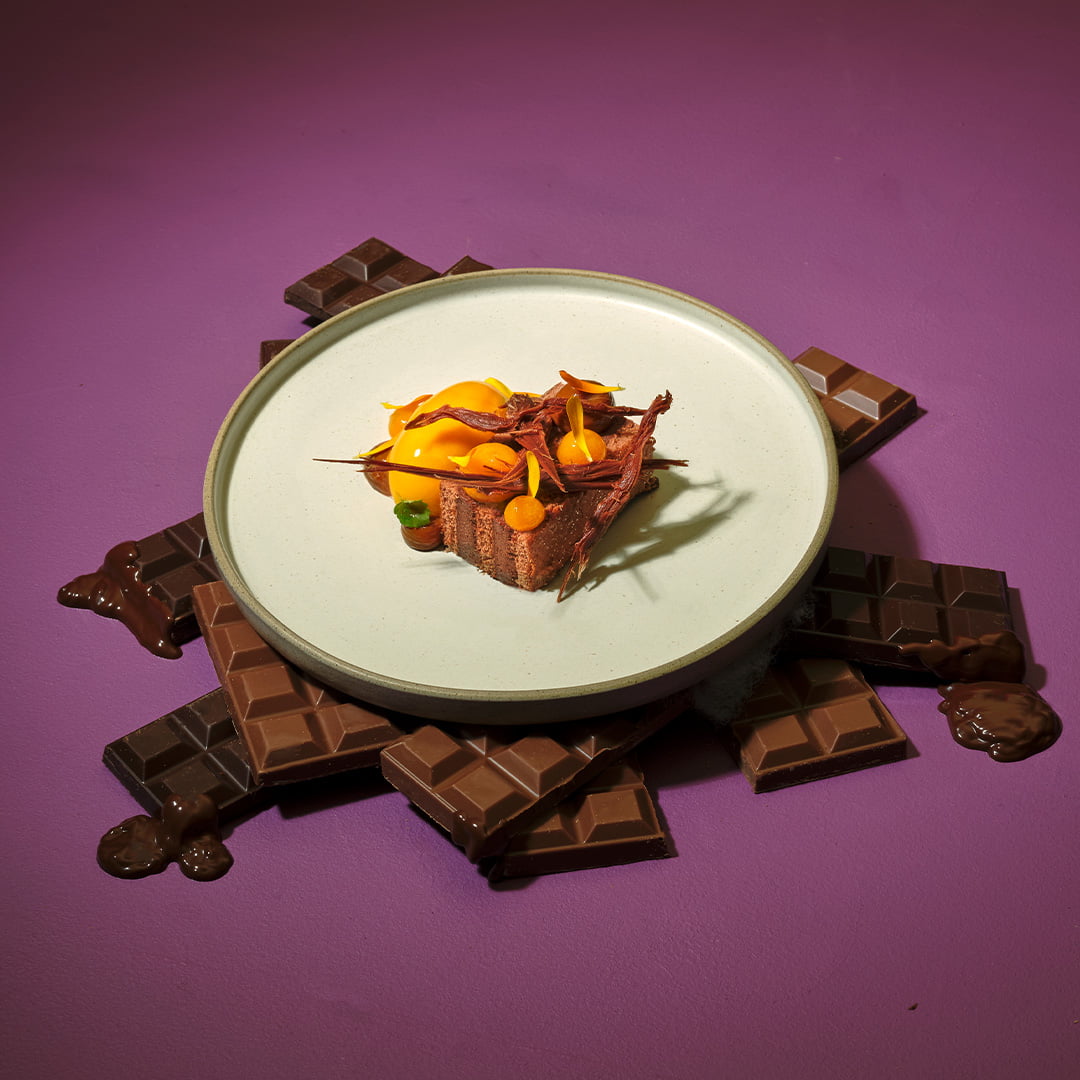 54% Chocolate Cremeux, Miso Caramel, Mango & Passion Fruit on a plate surrounded by blocks of chocolate.