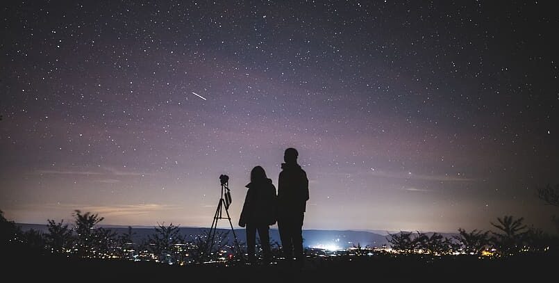 Two people watching a meteor shower on a hill. 