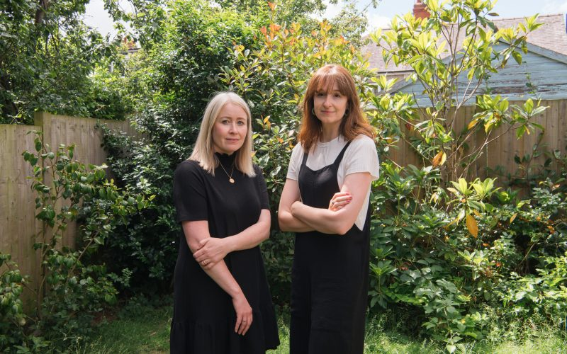 Two women smiling at the camera in a garden. 