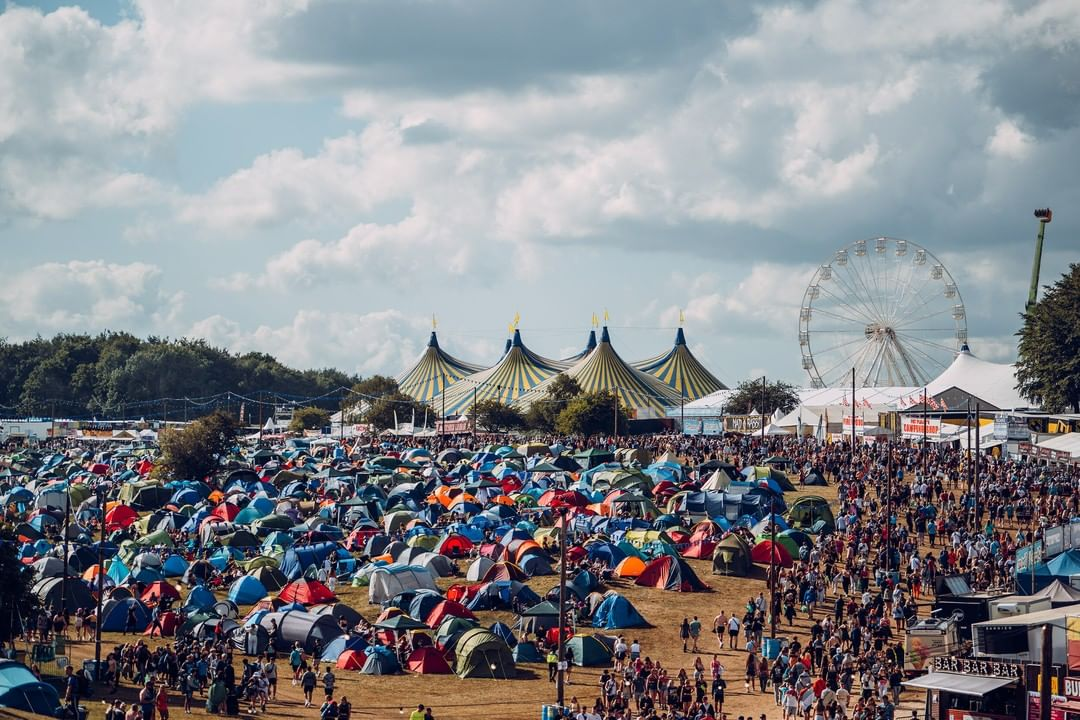 An aerial shot of a music festival with tents in the foreground and a ferris wheel in the background. 