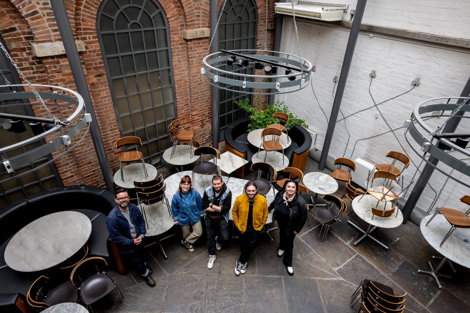 five people stood next to table and chairs inside an old building with exposed brick walls.