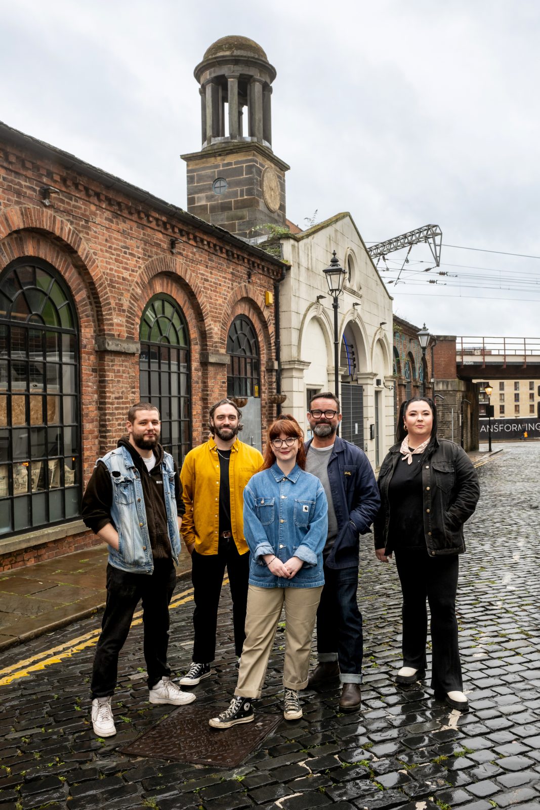 five people stood in the rain with an old cloth hall building behind them.