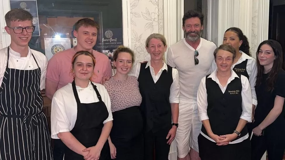 Hugh Jackman smiling for a photo with hotel staff.