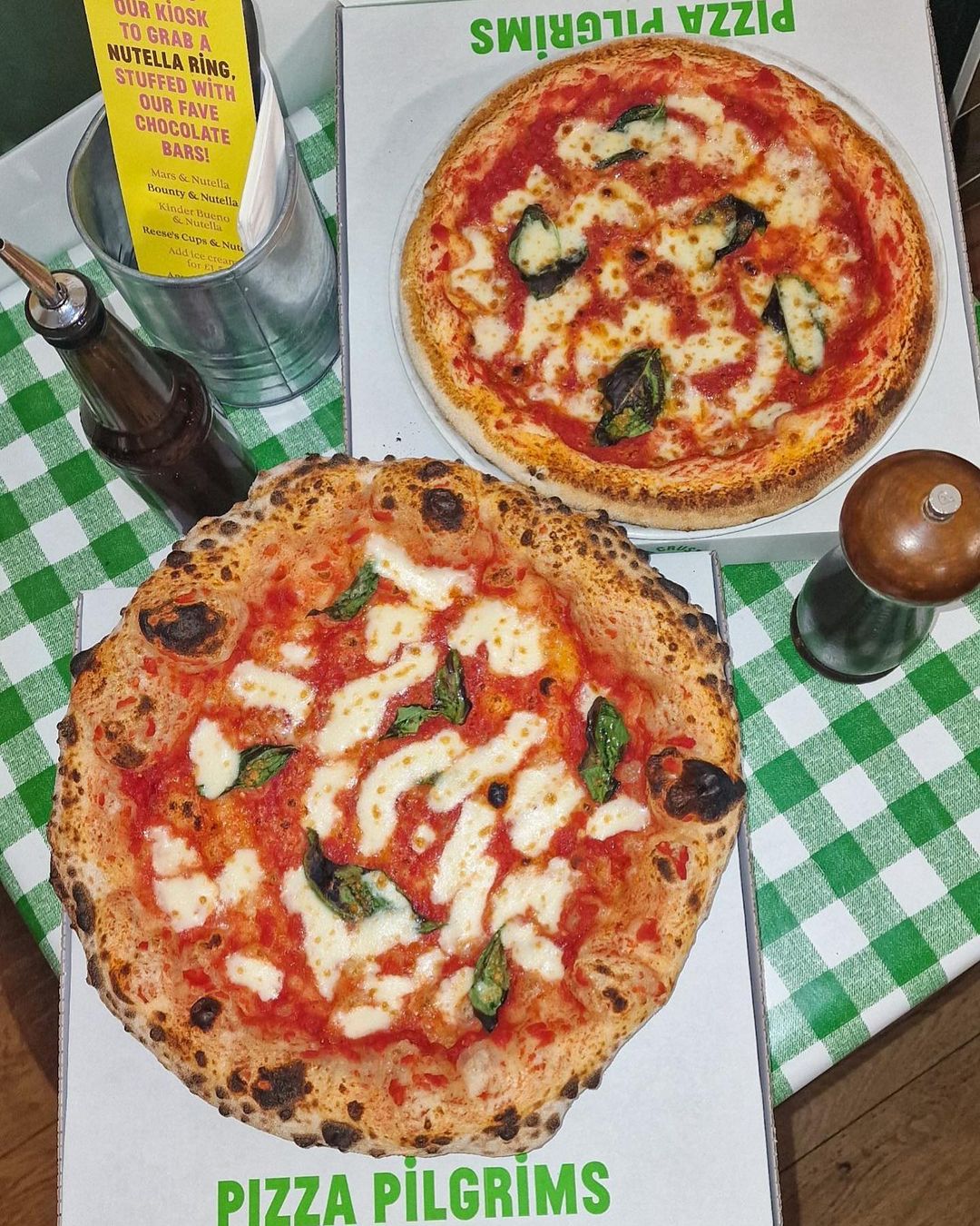 two margherita pizza, one normal base one gluten free on a green checkered table cloth.