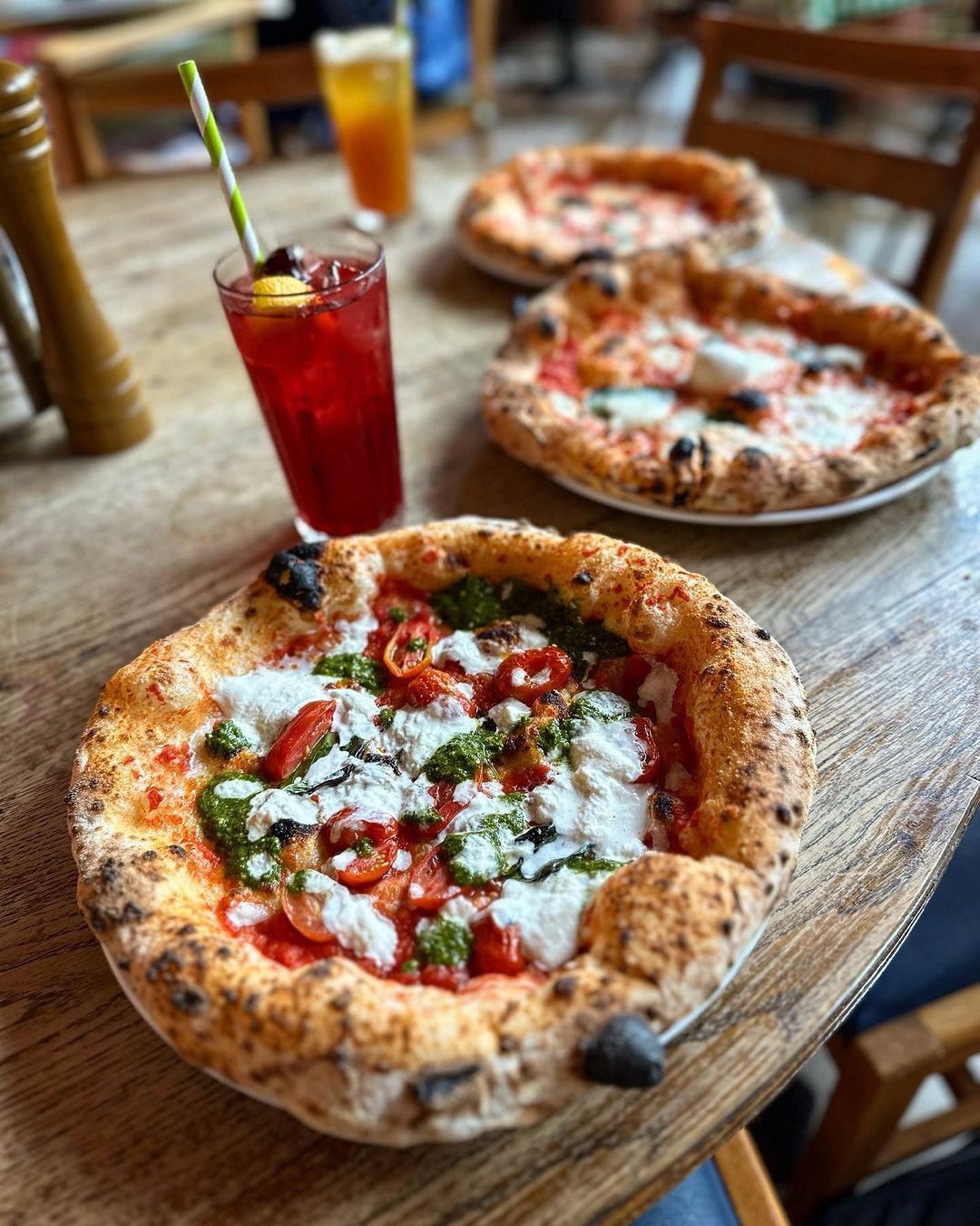 Three pizzas in a row on a wooden table.