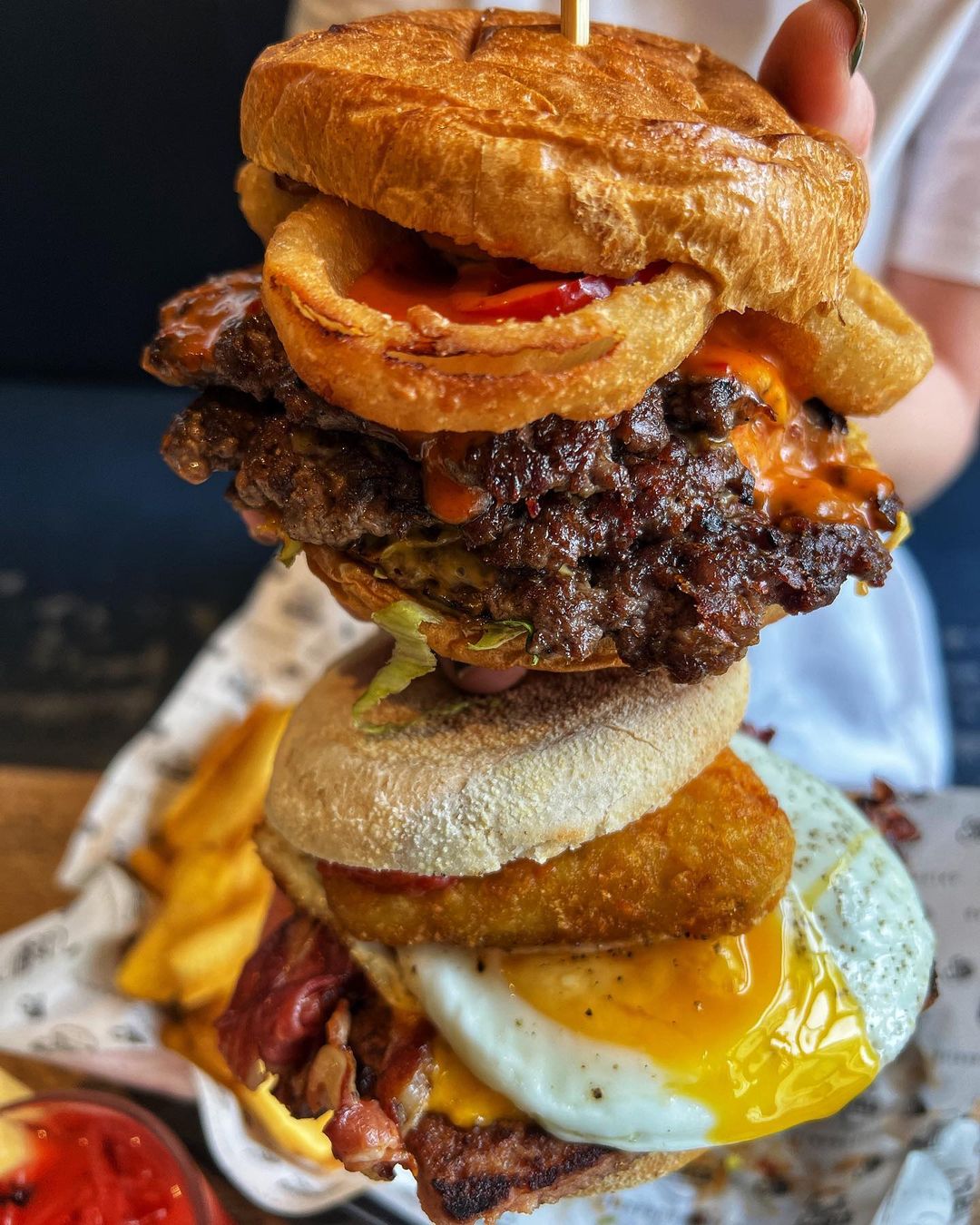 burger with an onion ring sticking out sat on top of a vegan muffin with scrambled tofu.