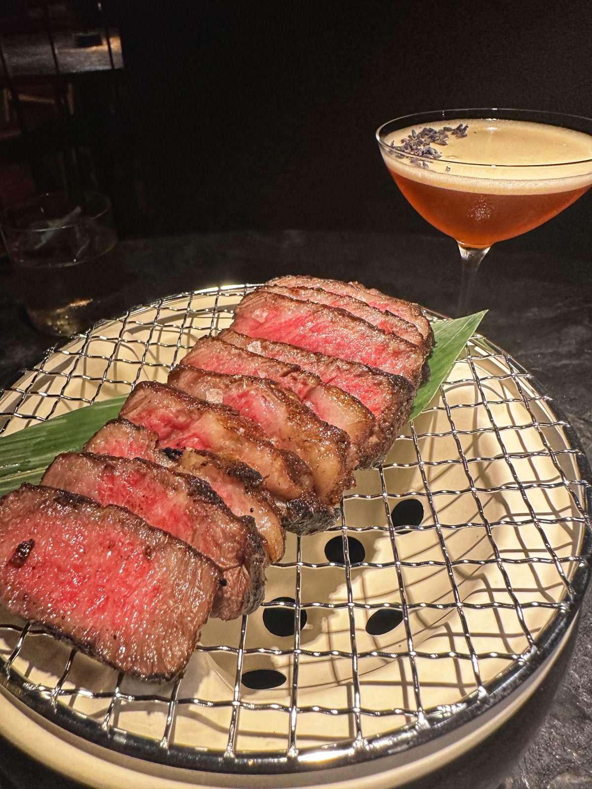 thinly sliced rare steak with orange cocktail in the background.