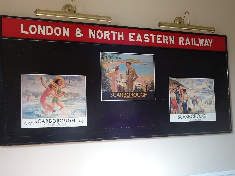 old station board reading 'London and North Eastern Railway' with posters of Scarborough.