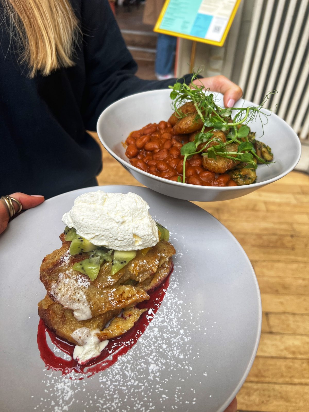 two plates held in each hand. One with pancakes another with beans.