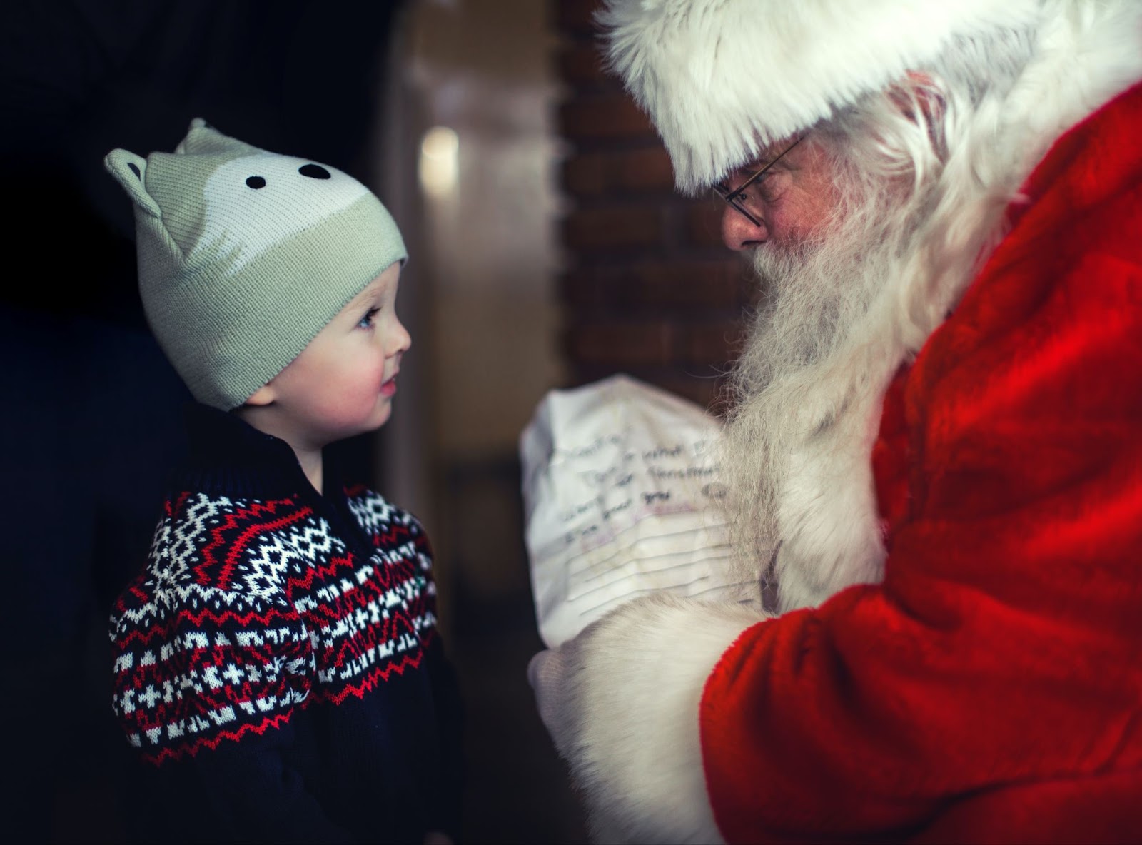 Santa with a list next to young boy in a fox hat and Christmas jumper.