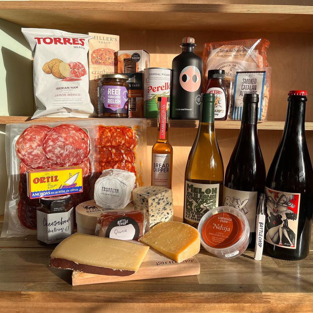 bottles of wine with cheese, torres crisps and olive jars.