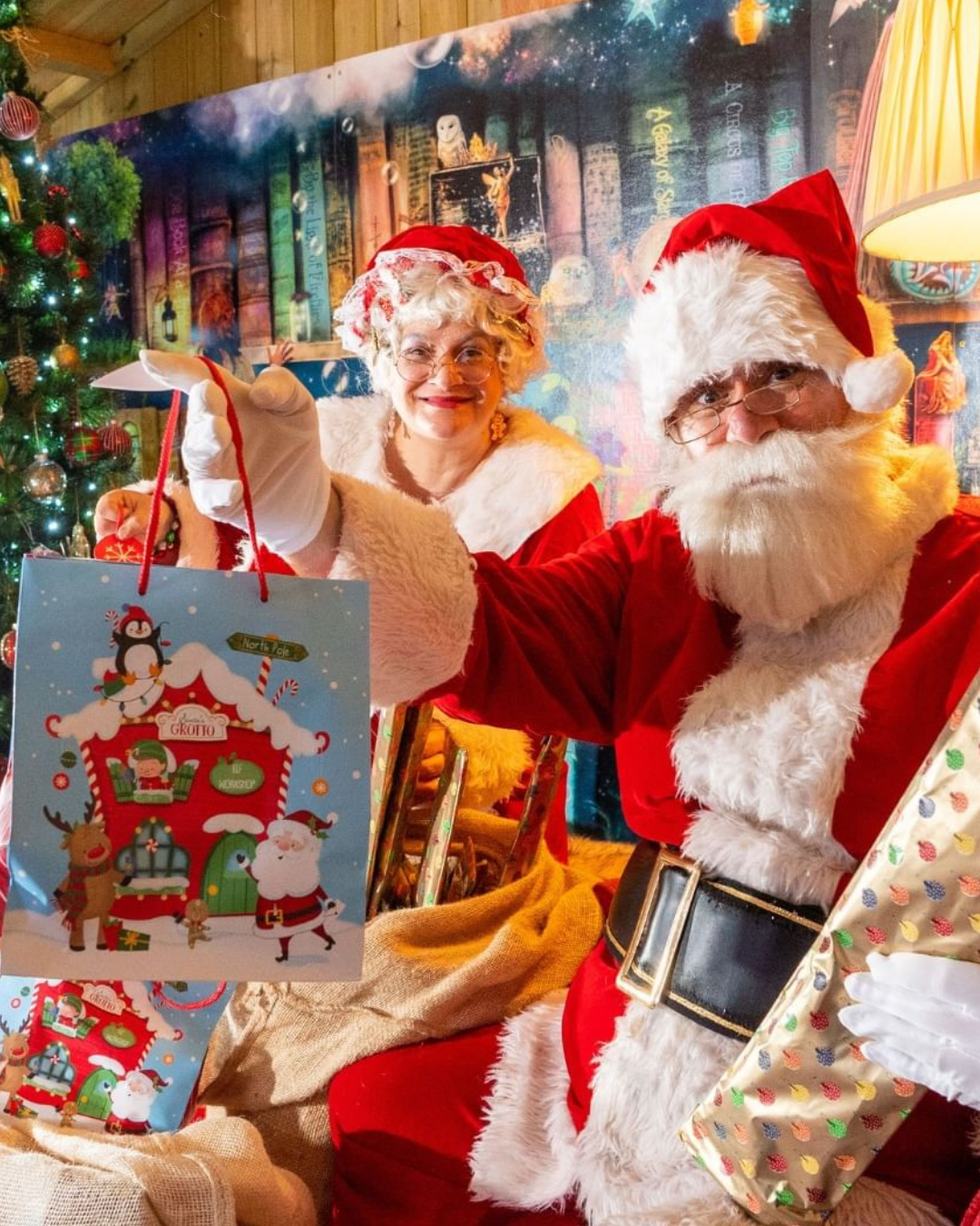 santa and mrs claus holding up a christmas shopping bag.