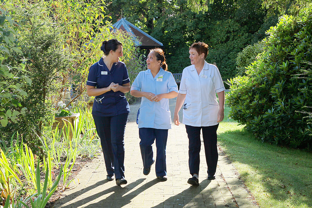 Three nurses from St Gemma's Hospice walking in a garden. 