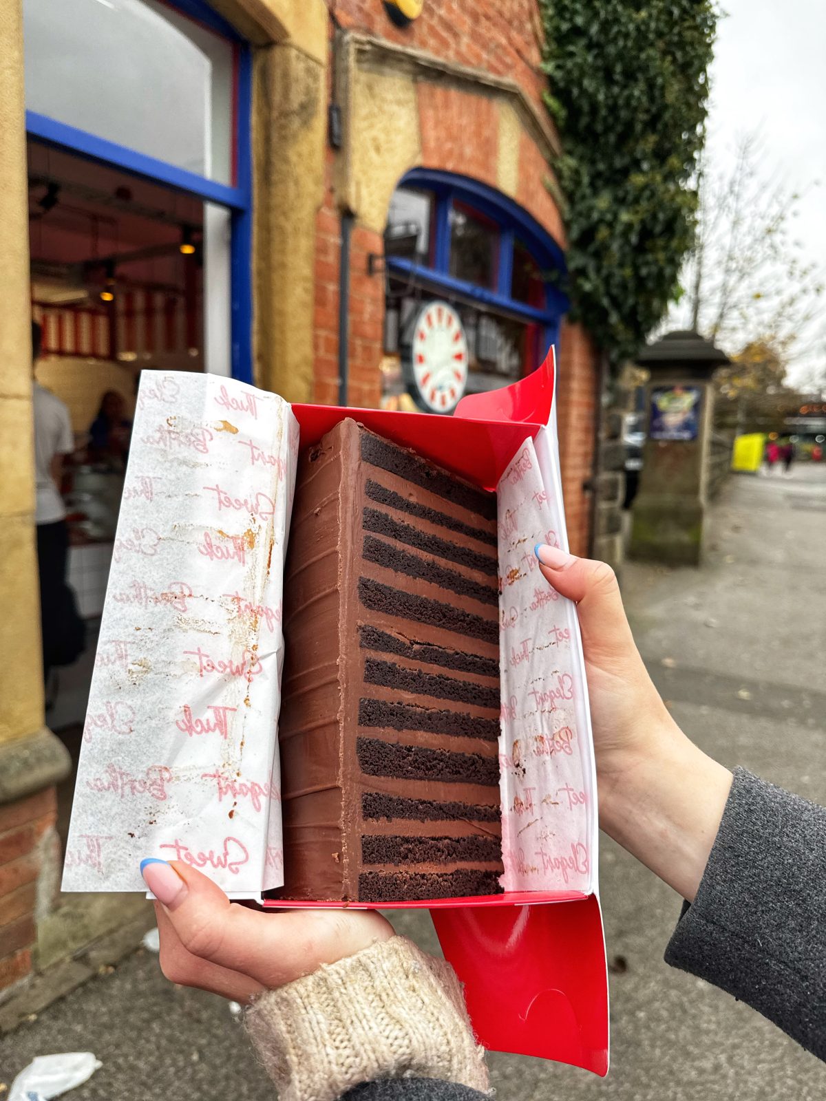 A slice of chocolate cake being held up outside Get Baked in Headingley.